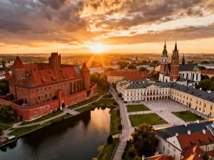 Zabytkowy drewniany kościół z gontowym dachem, otoczony zieloną łąką i lasem w promieniach zachodzącego słońca.