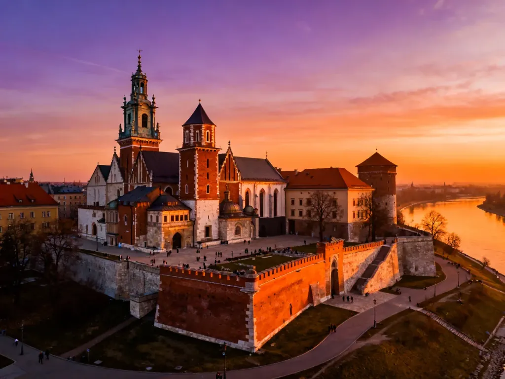 Zamek Królewski na Wawelu w Krakowie o zachodzie słońca, malowniczo odbijający się w wodach Wisły.