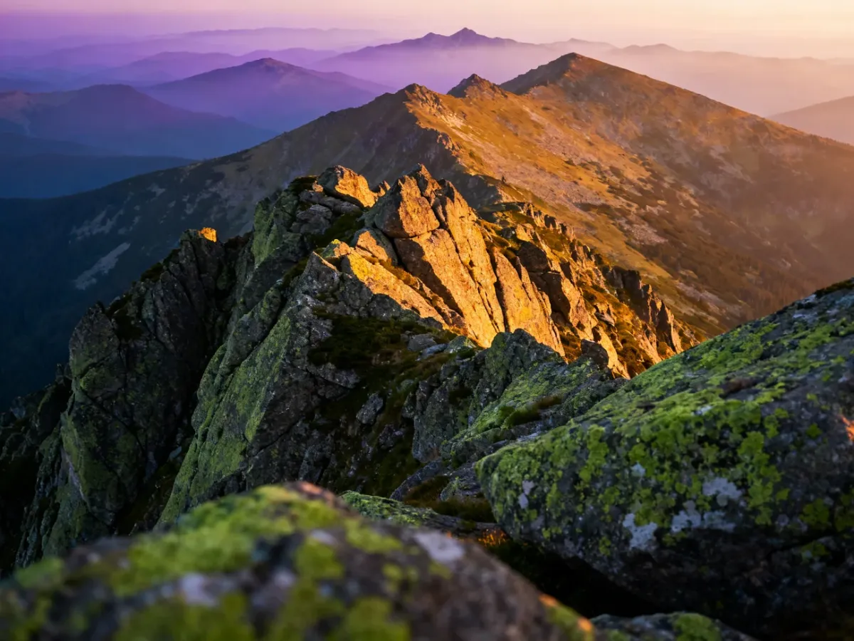 Panoramiczny widok na szczyty Karkonoszy o zachodzie słońca z wyraźnymi formacjami skalnymi na pierwszym planie.